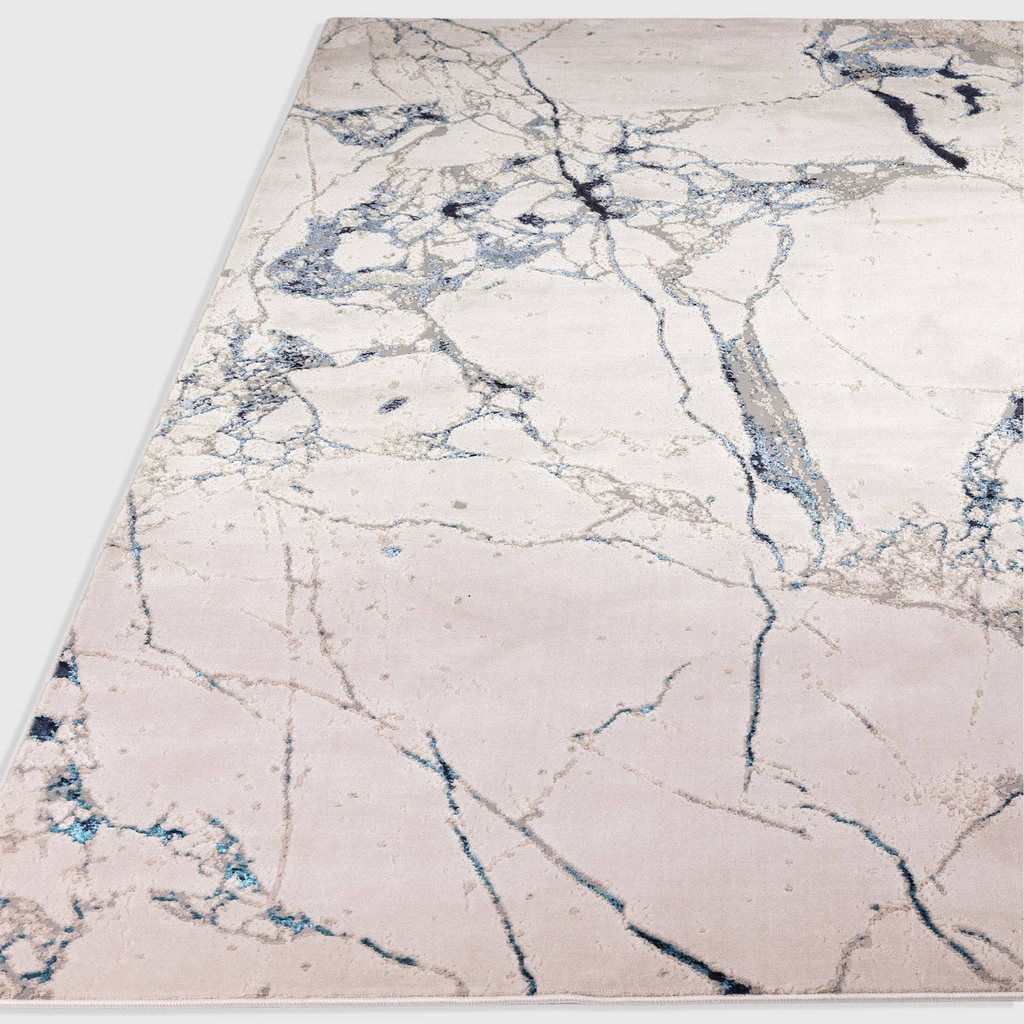 Alvo Rugs Aurorella Quake Au22 abstract area rug with blue and grey marble-inspired patterns on a soft cream base.