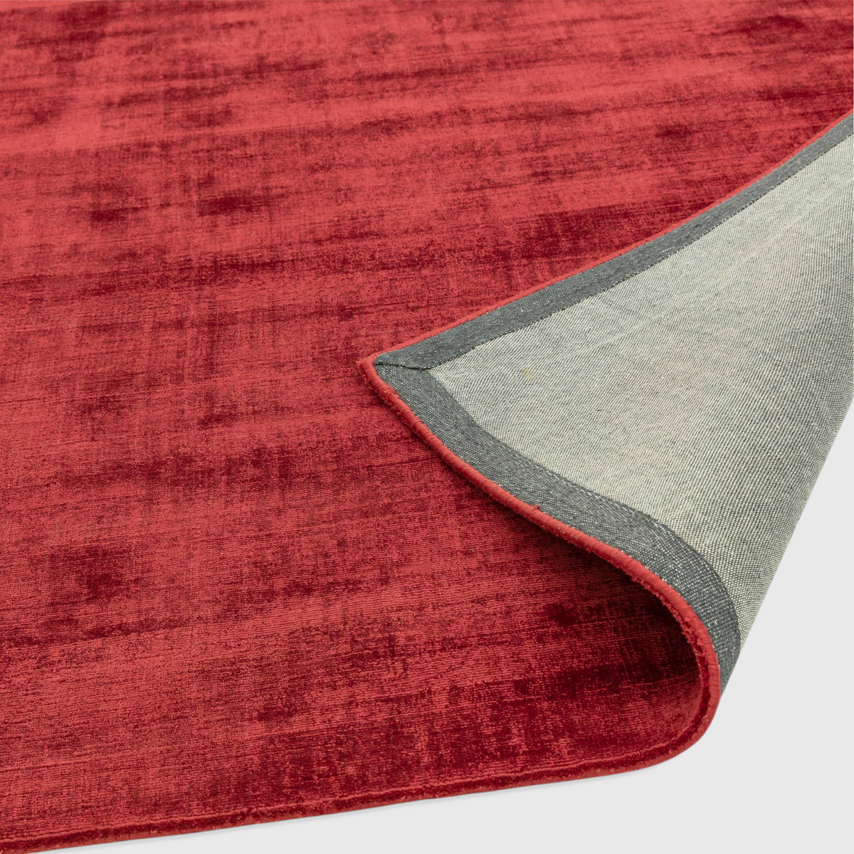 Alvo Rugs Blayde Berry hand-woven viscose rug in deep red with a folded corner showing the grey backing