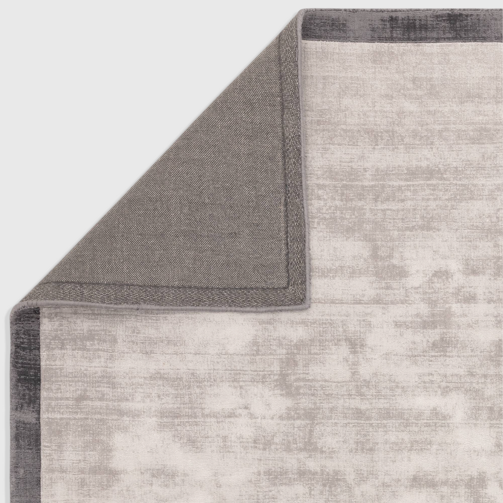 Alvo Rugs Blayde silver and grey viscose rug showing the hand-woven texture and dark border detail from the corner.