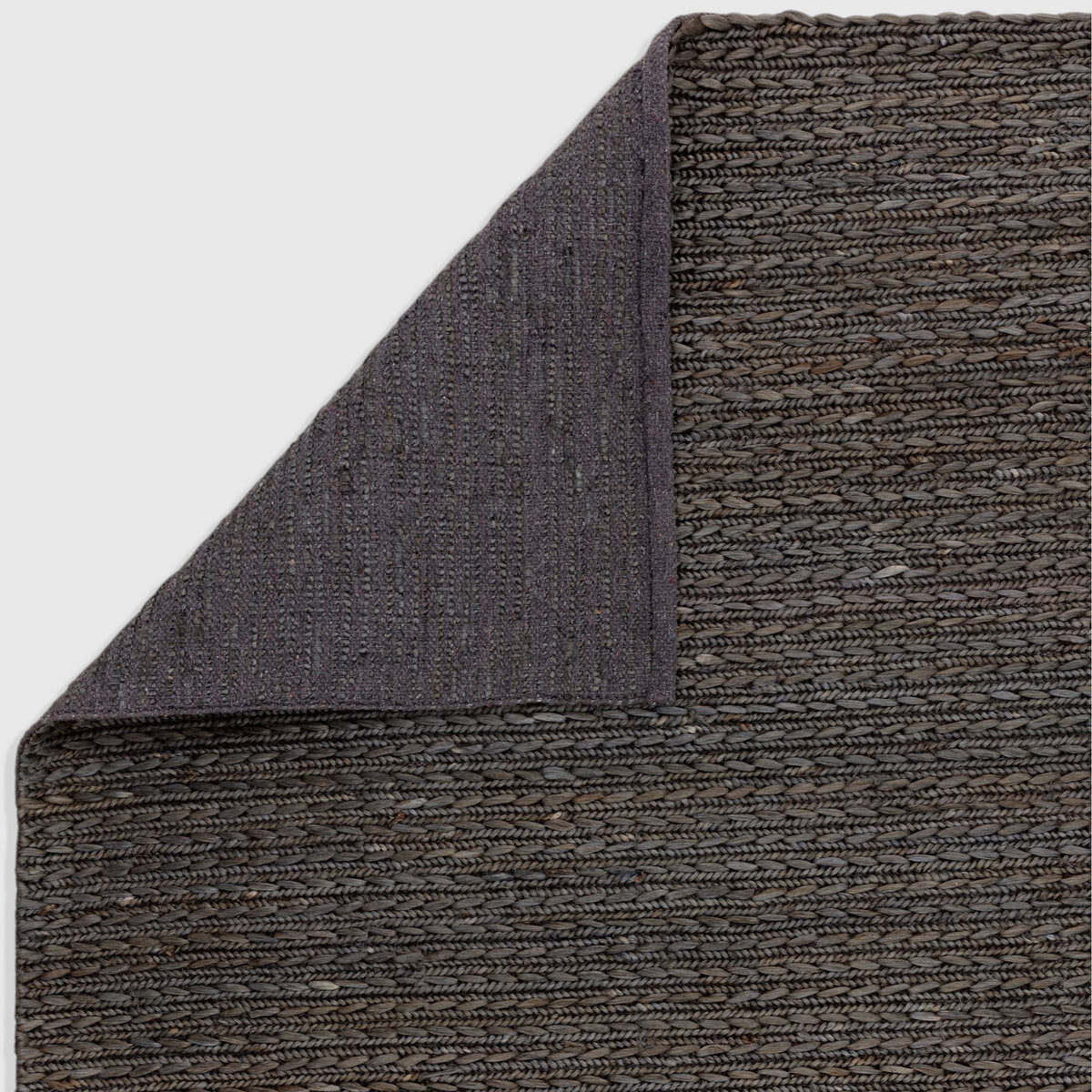 Alvo Rugs Oaks charcoal hand-woven flatweave rug showing the textured jute surface and cotton backing corner fold.