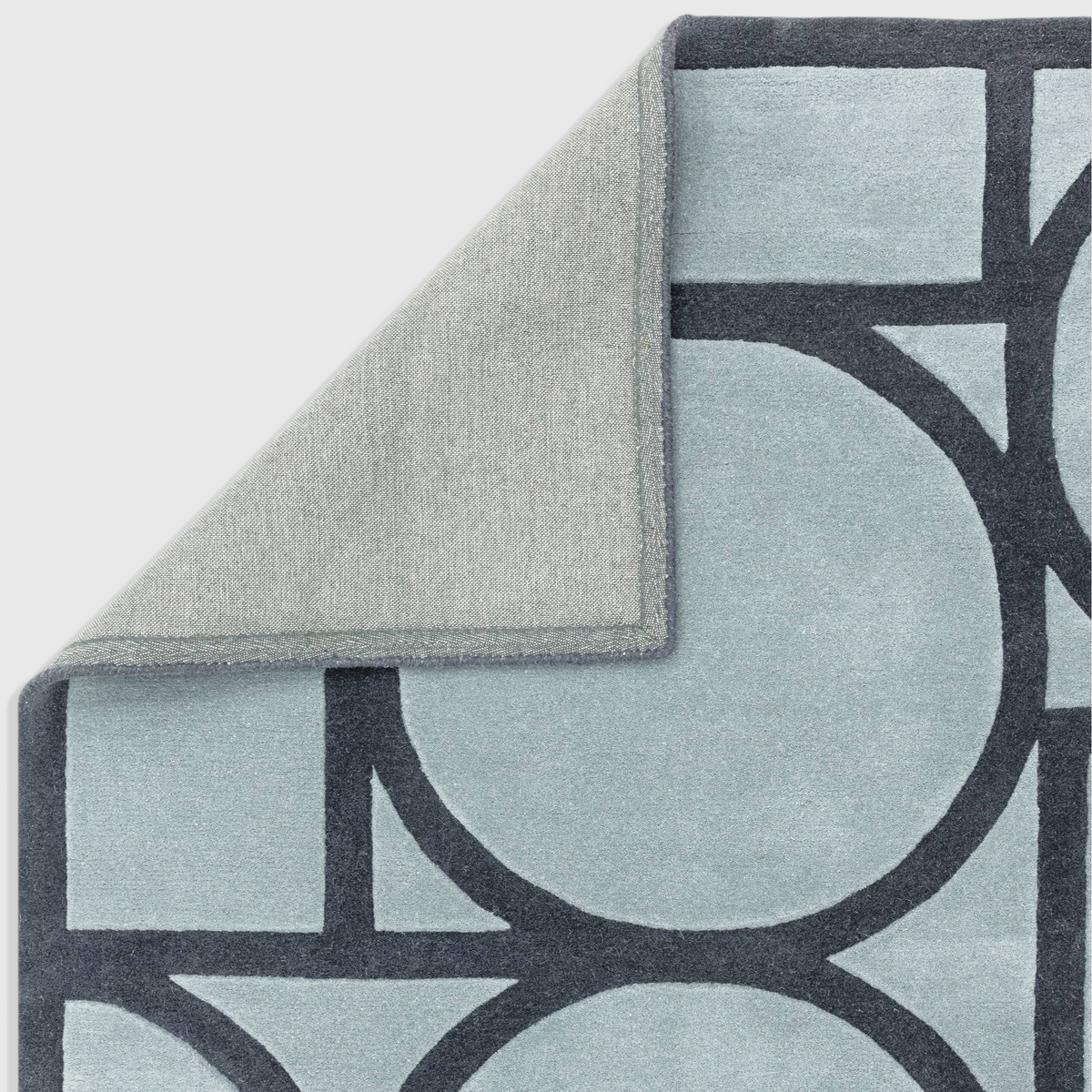 Alvo Rugs Metra blue wool rug with geometric pattern and hand tufted high low pile showing cotton backing corner
