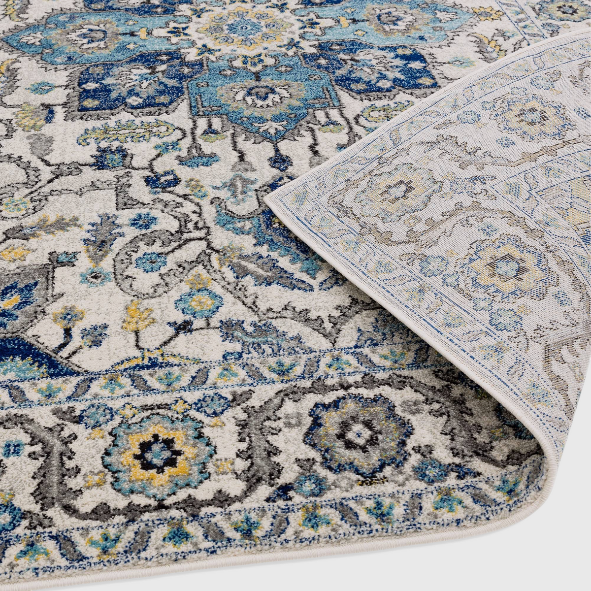 Alvo Rugs Novella Nv25 Persian blue rug with intricate floral patterns and a folded corner showing the jute backing.