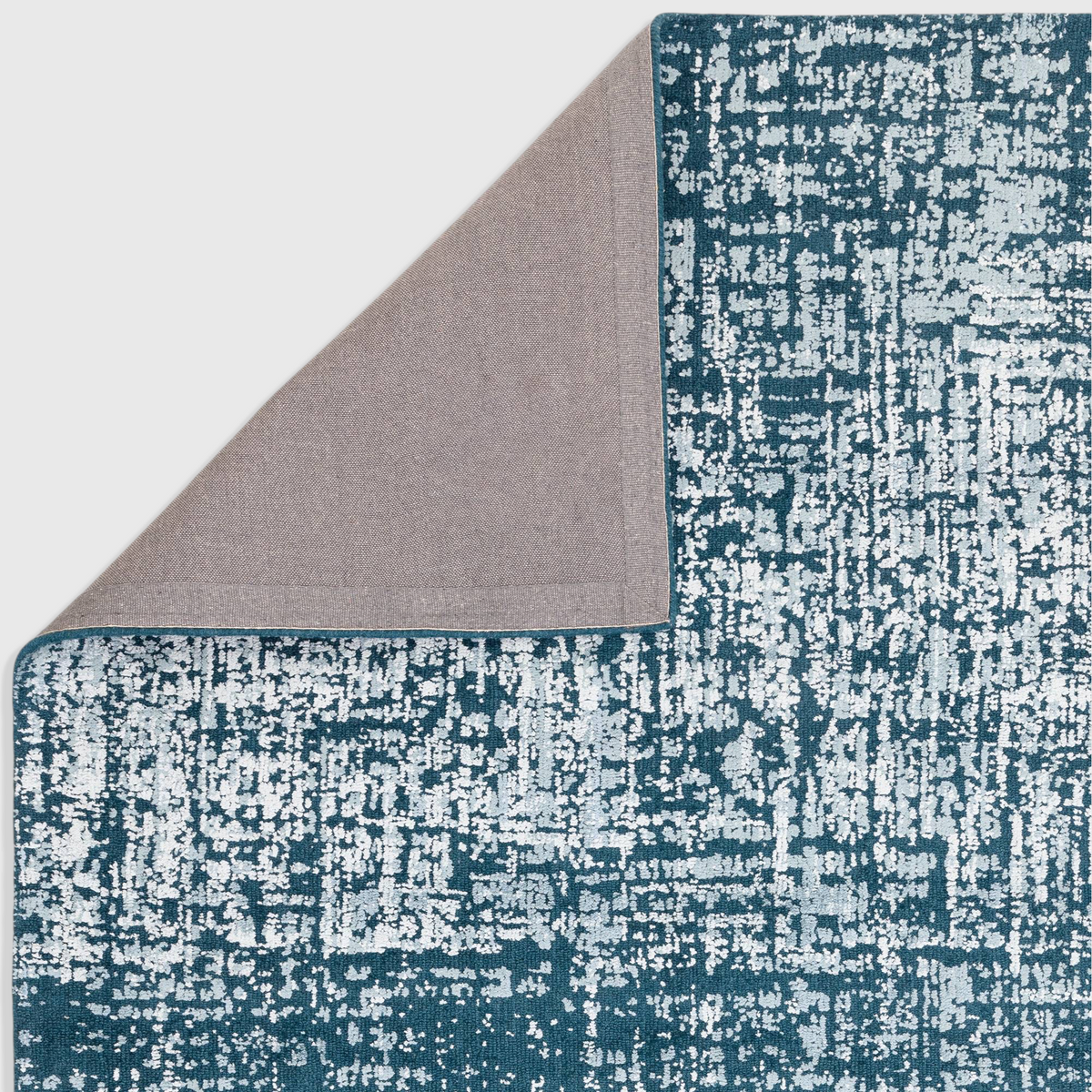 Alvo Rugs Torina teal green abstract rug with a folded corner showing the grey cotton and latex backing